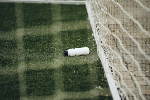 A white water bottle on a green soccer field near the goal net, suggesting a sports setting.