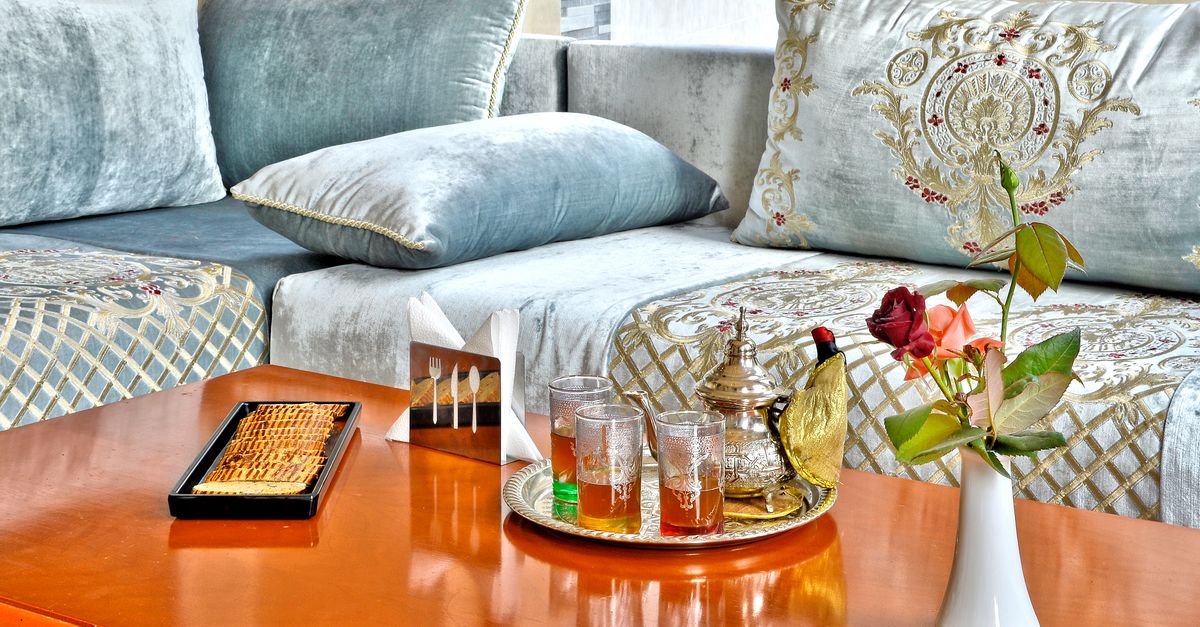 Elegant Moroccan tea setup with ornate pillows, teapot, and mint tea on a wooden table in Fès.