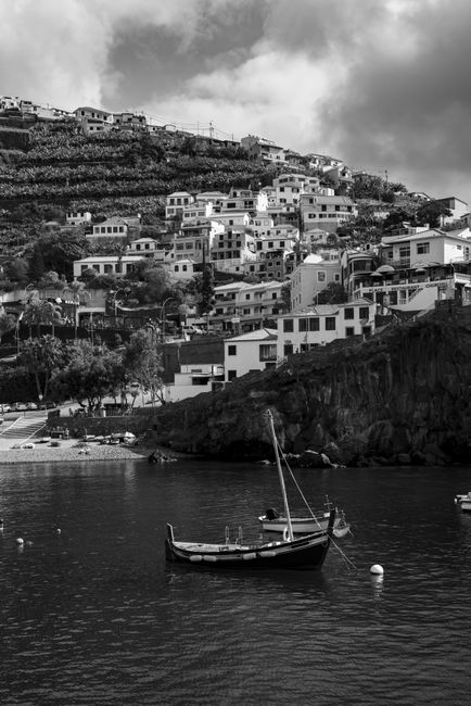 Black and white image of a serene coastal village in Madeira, Portugal with boats on the water.