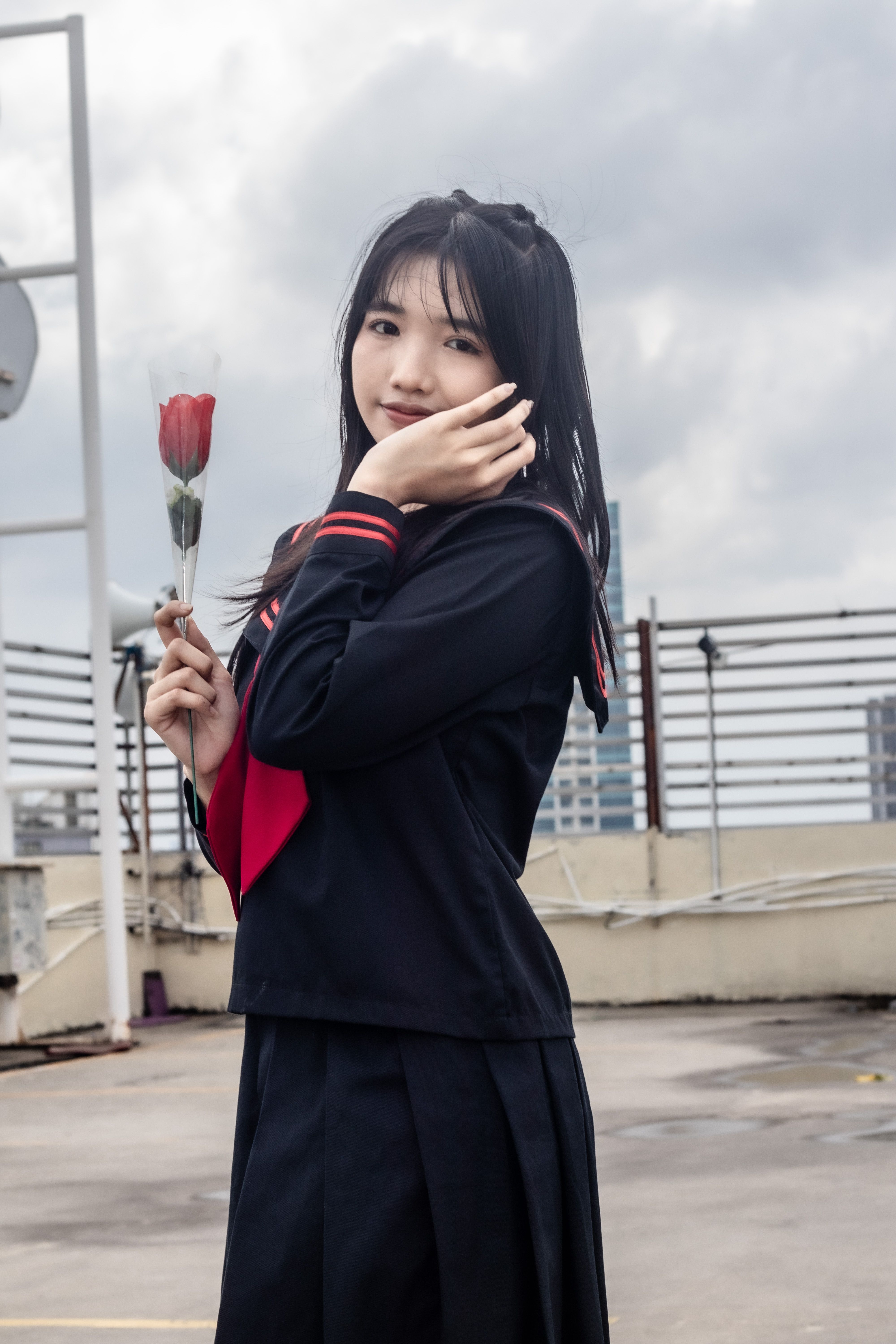 Portrait of a young woman in a school uniform holding a rose on a rooftop.
