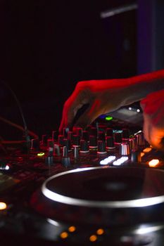 Close-up of DJ hands mixing music on a console, illuminated by vibrant lights.