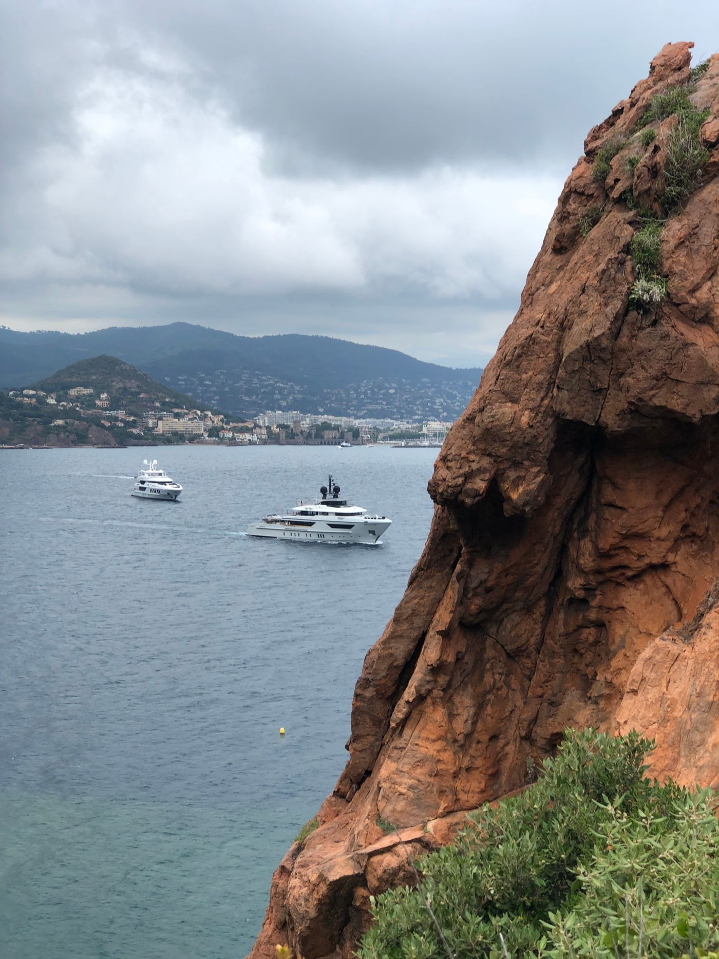 Two superyachts cruising beneath red coastal cliffs