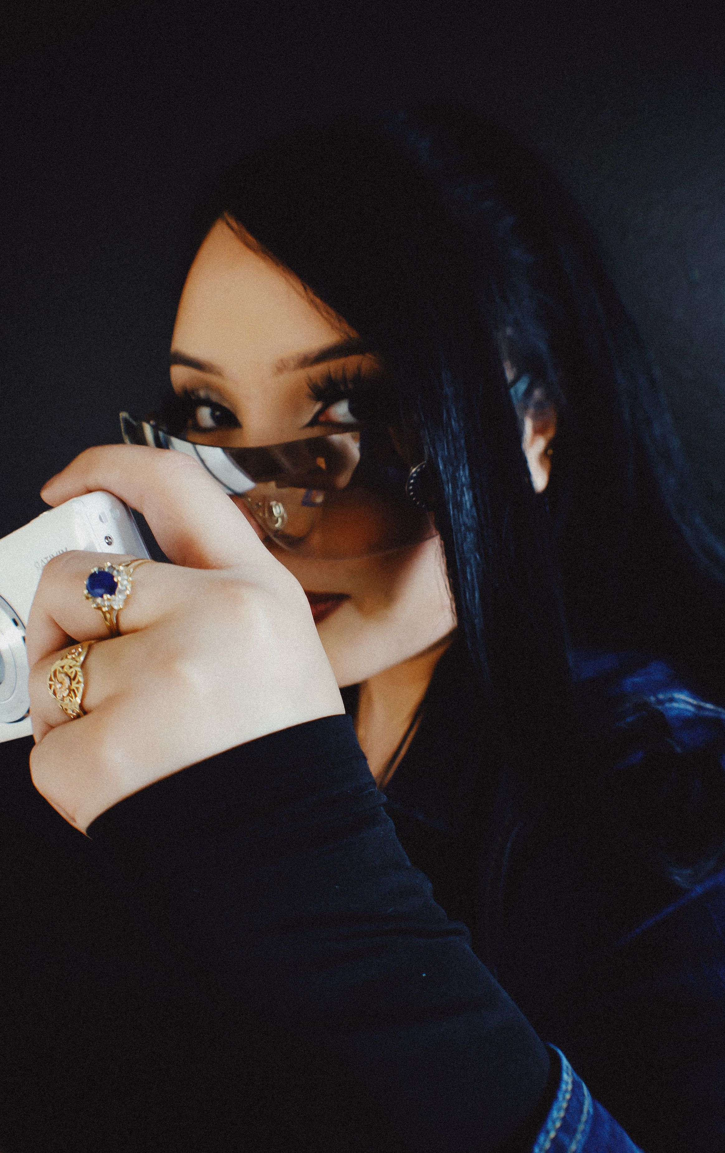 Woman with elegant rings holding a camera, creating an air of mystery in a dark setting.