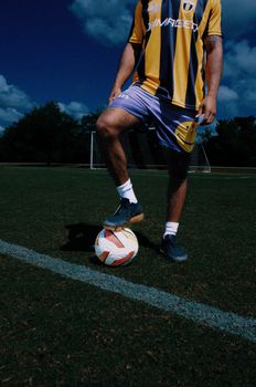 Man in soccer uniform standing on grassy field with football, ready to play.