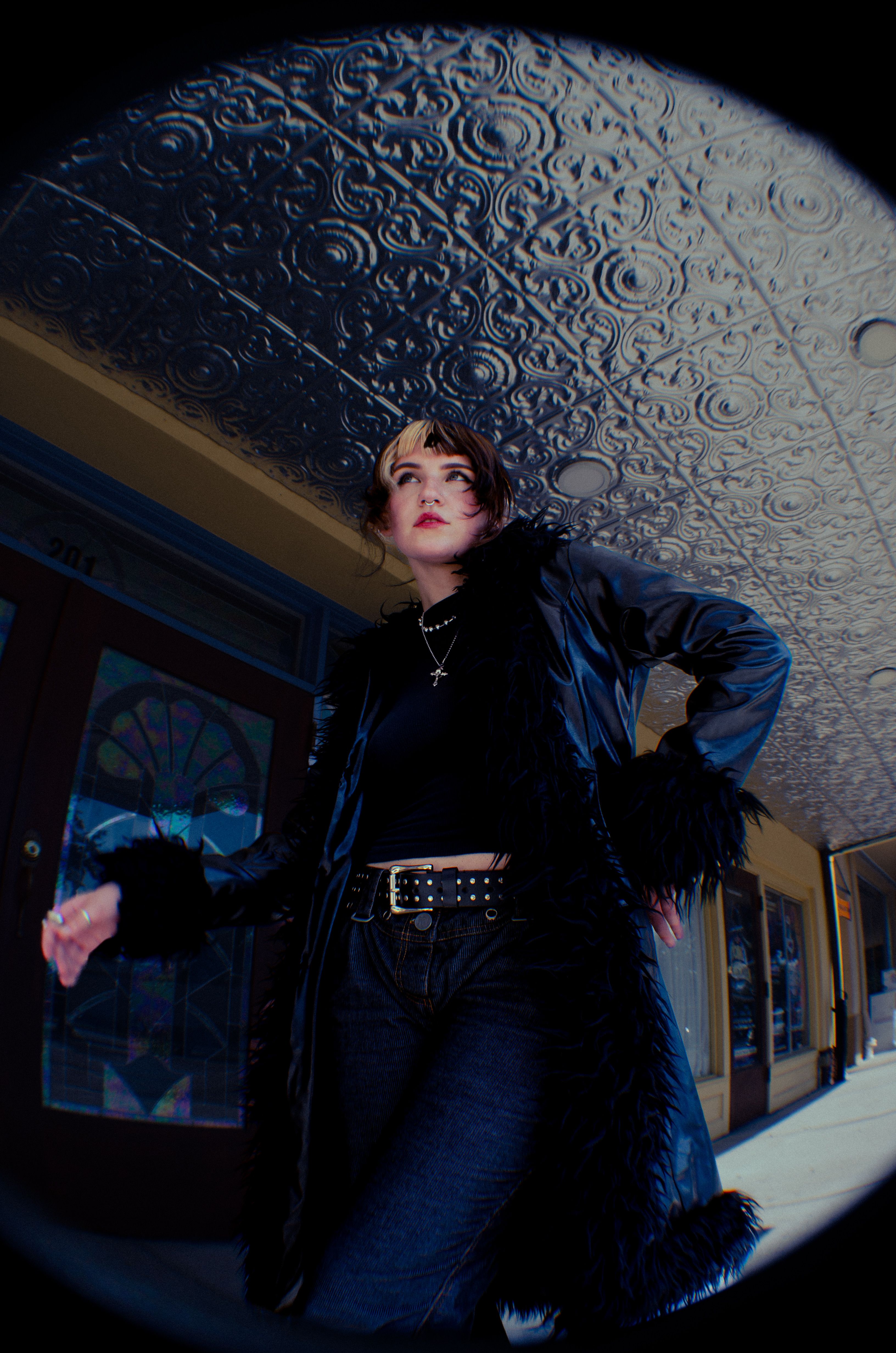 Stylish woman in a black coat poses dramatically in a vintage urban setting.