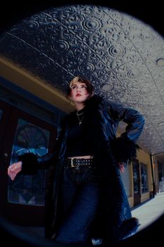 Stylish woman in a black coat poses dramatically in a vintage urban setting.