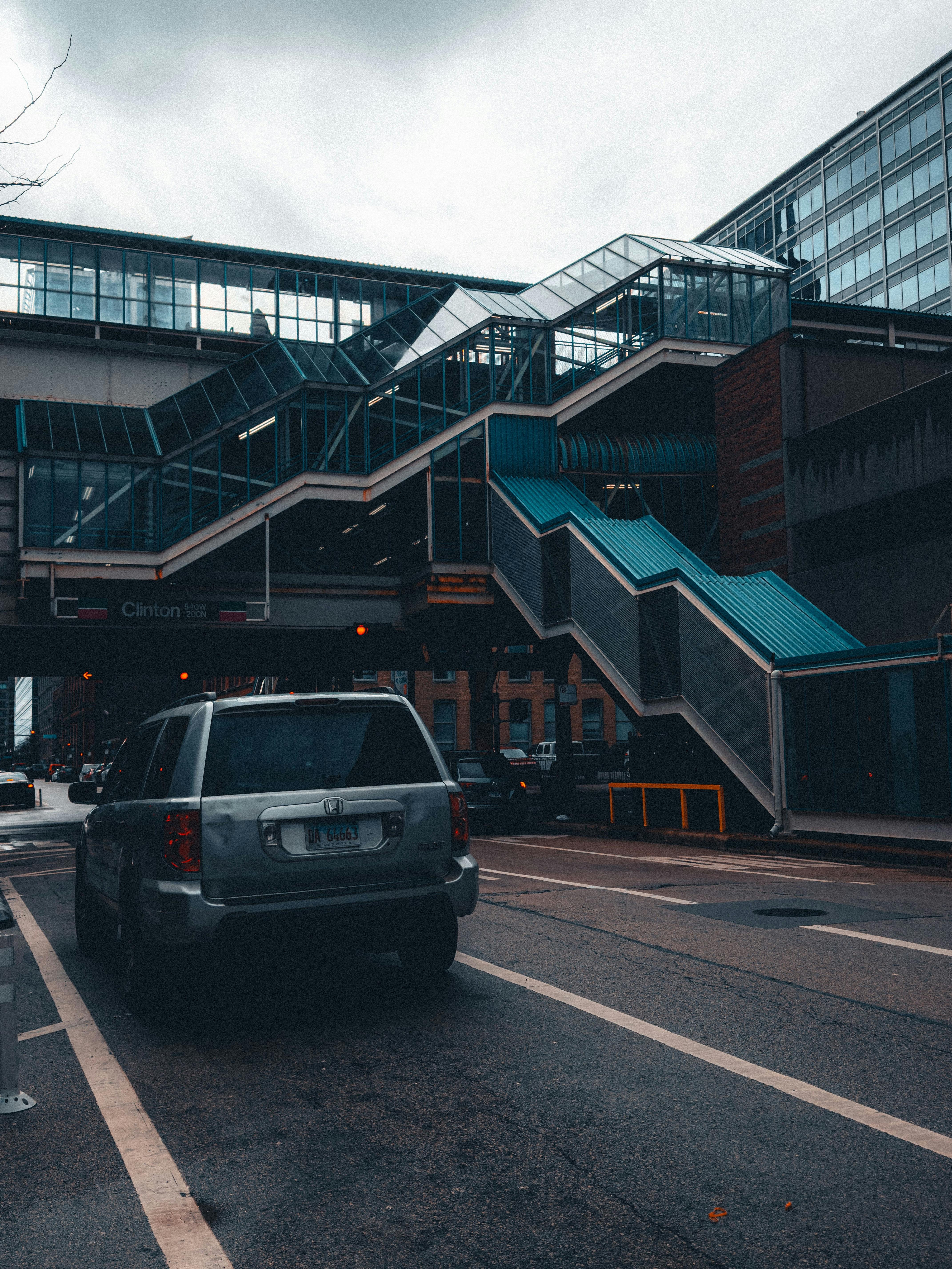 Urban transit station with geometric glass stairs and cars on a cloudy day.