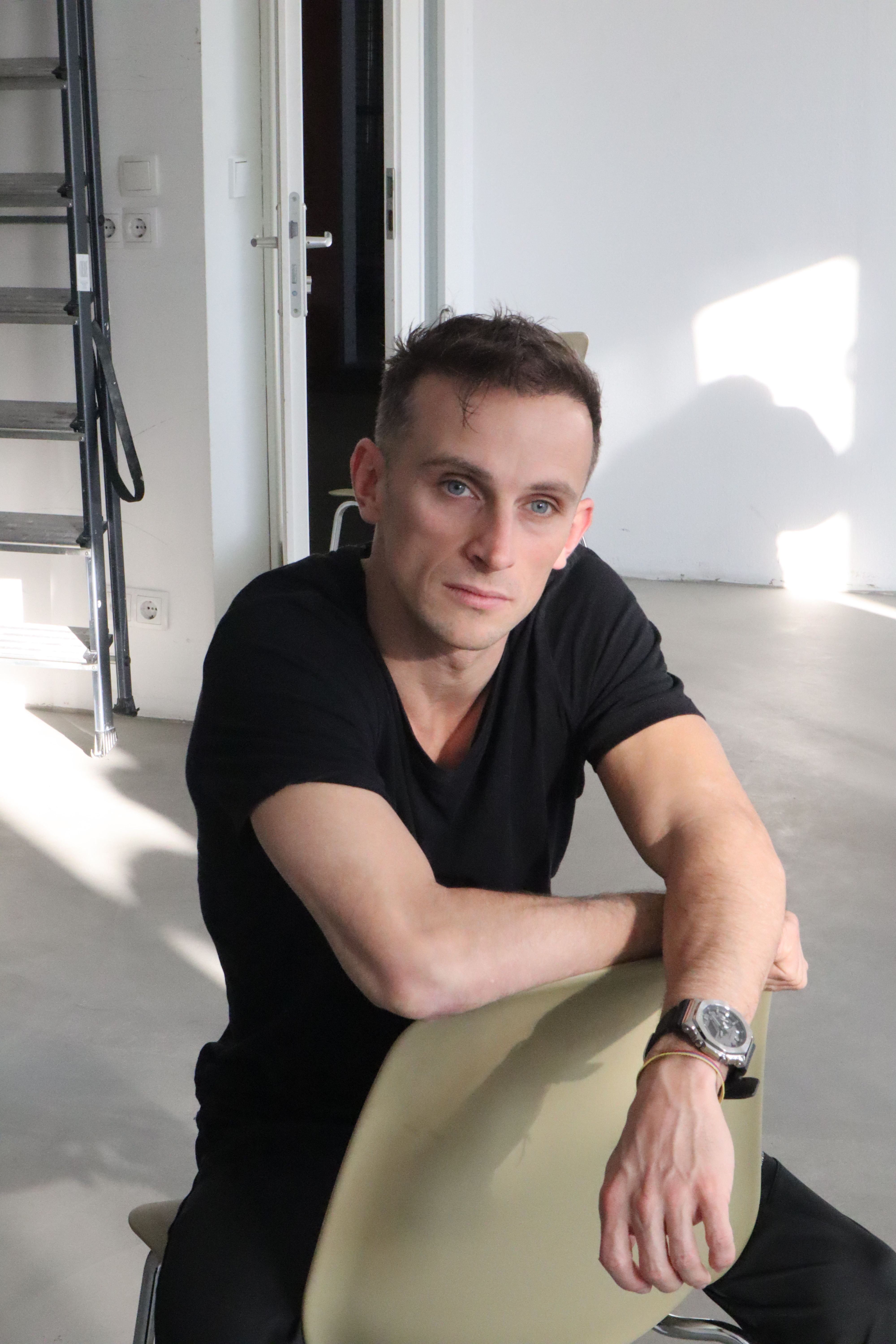 A young man sits casually on a chair in a bright modern room, showcasing a minimalist style.