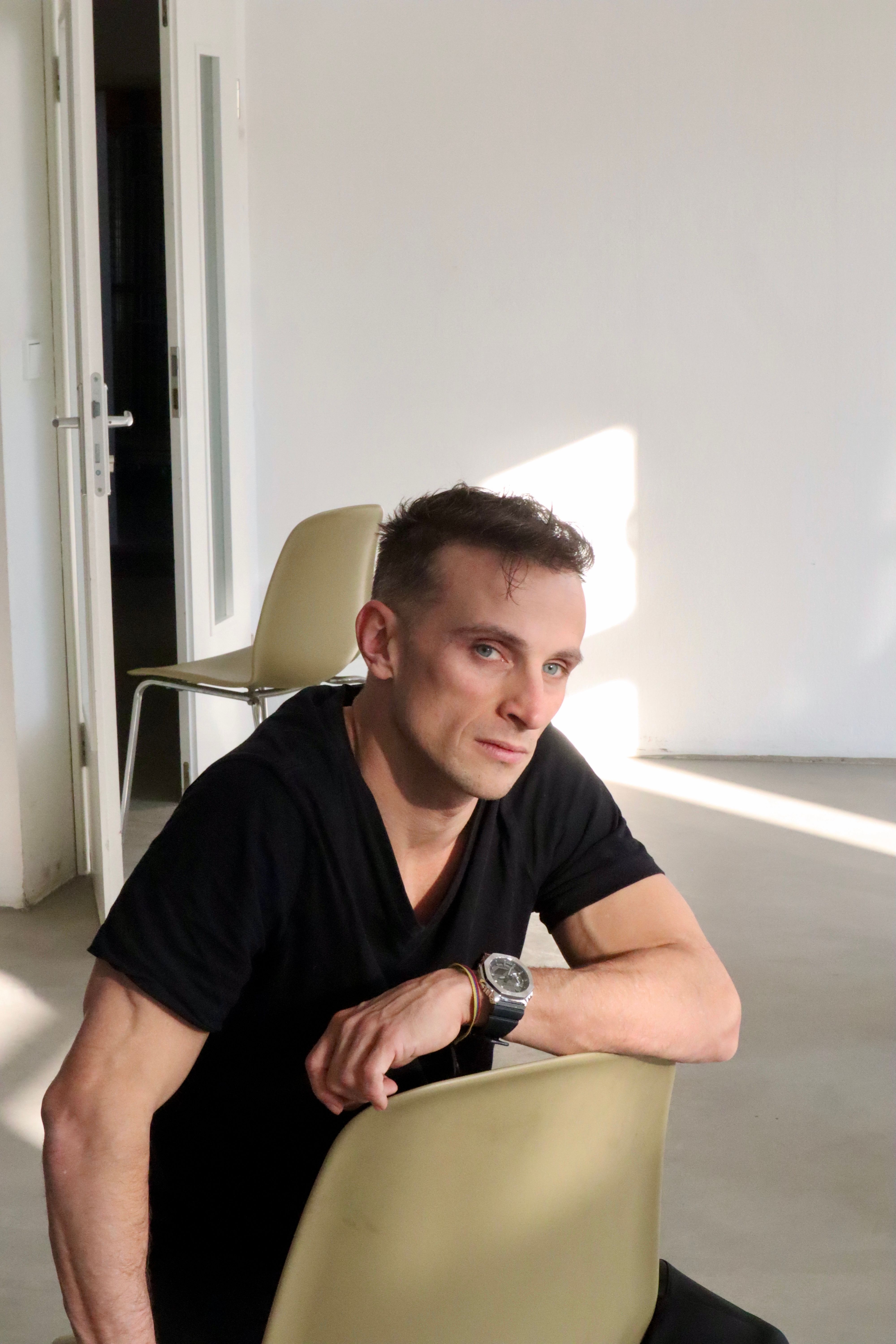 Young man sitting on a chair, bathed in natural light, interior setting.