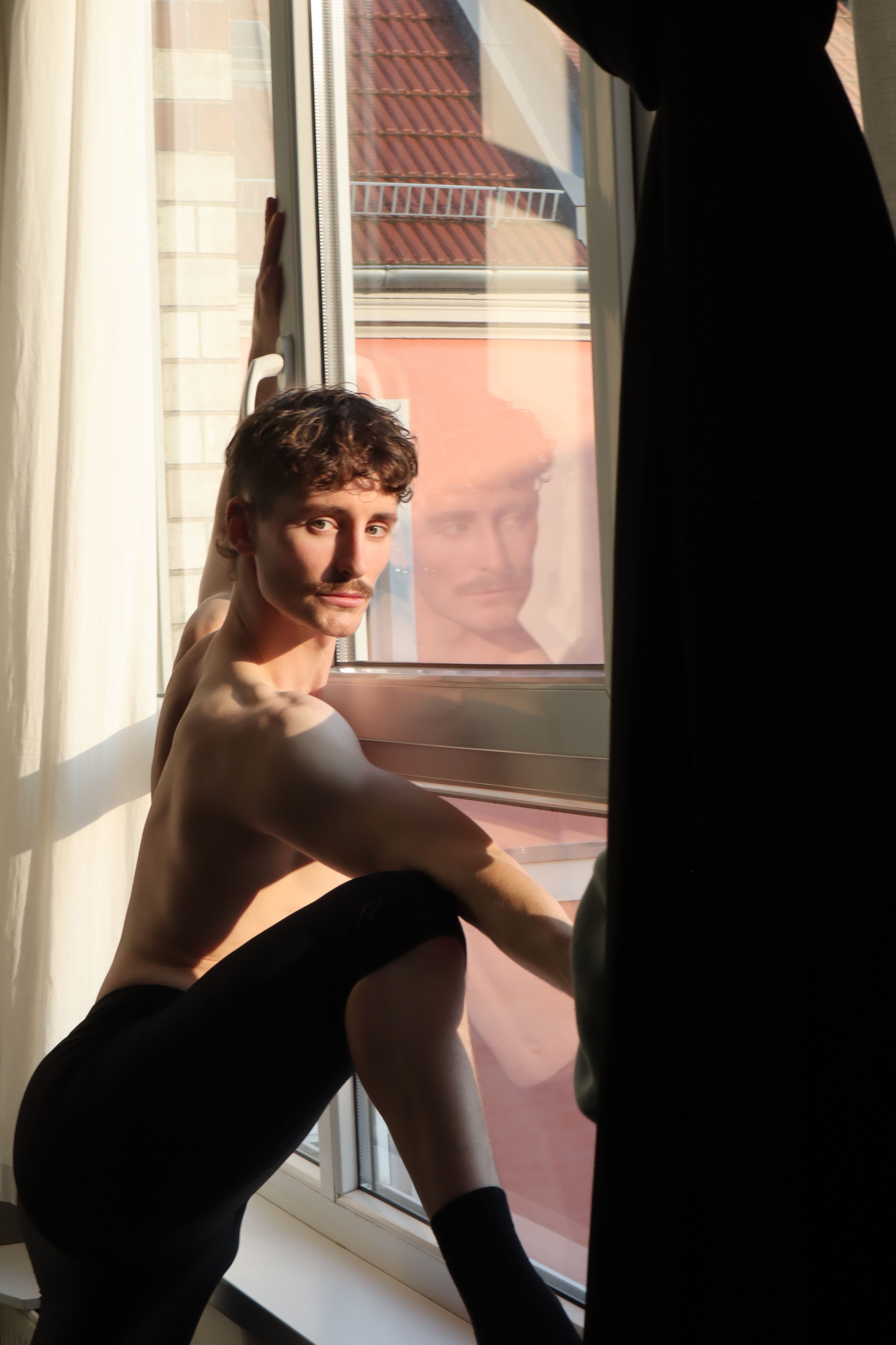 Young male dancer posing by a window in Berlin, showcasing graceful contemporary movement.