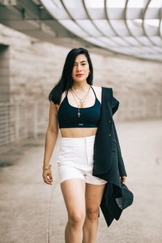 Stylish woman in black top and white shorts walking confidently in an urban environment.