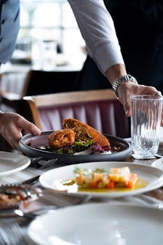 A waiter serves a plate of crispy fried chicken with mixed vegetables at a restaurant table.