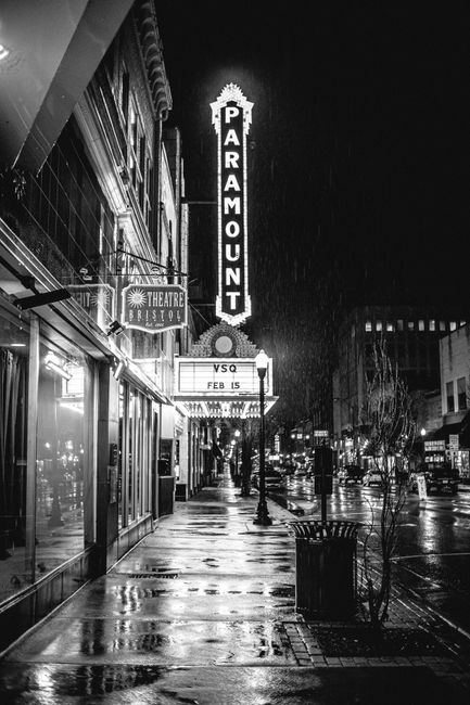 Black and white photo of Paramount Theatre at night with rain-soaked street, creating a dramatic atmosphere.