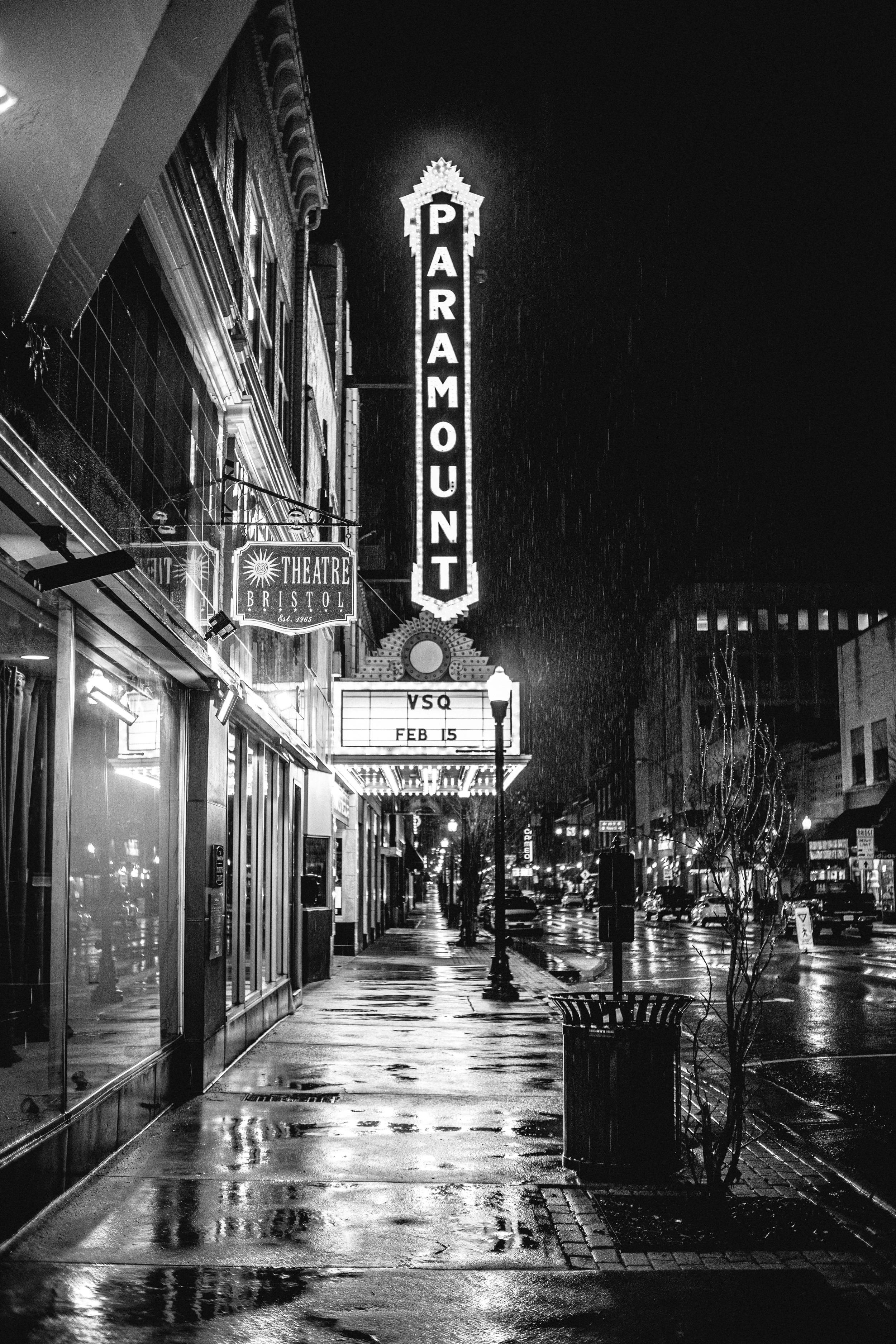 bezplatná Černobílá fotografie divadla Paramount v noci s deštěm nasáklou ulicí, která vytváří dramatickou atmosféru. Základová fotografie