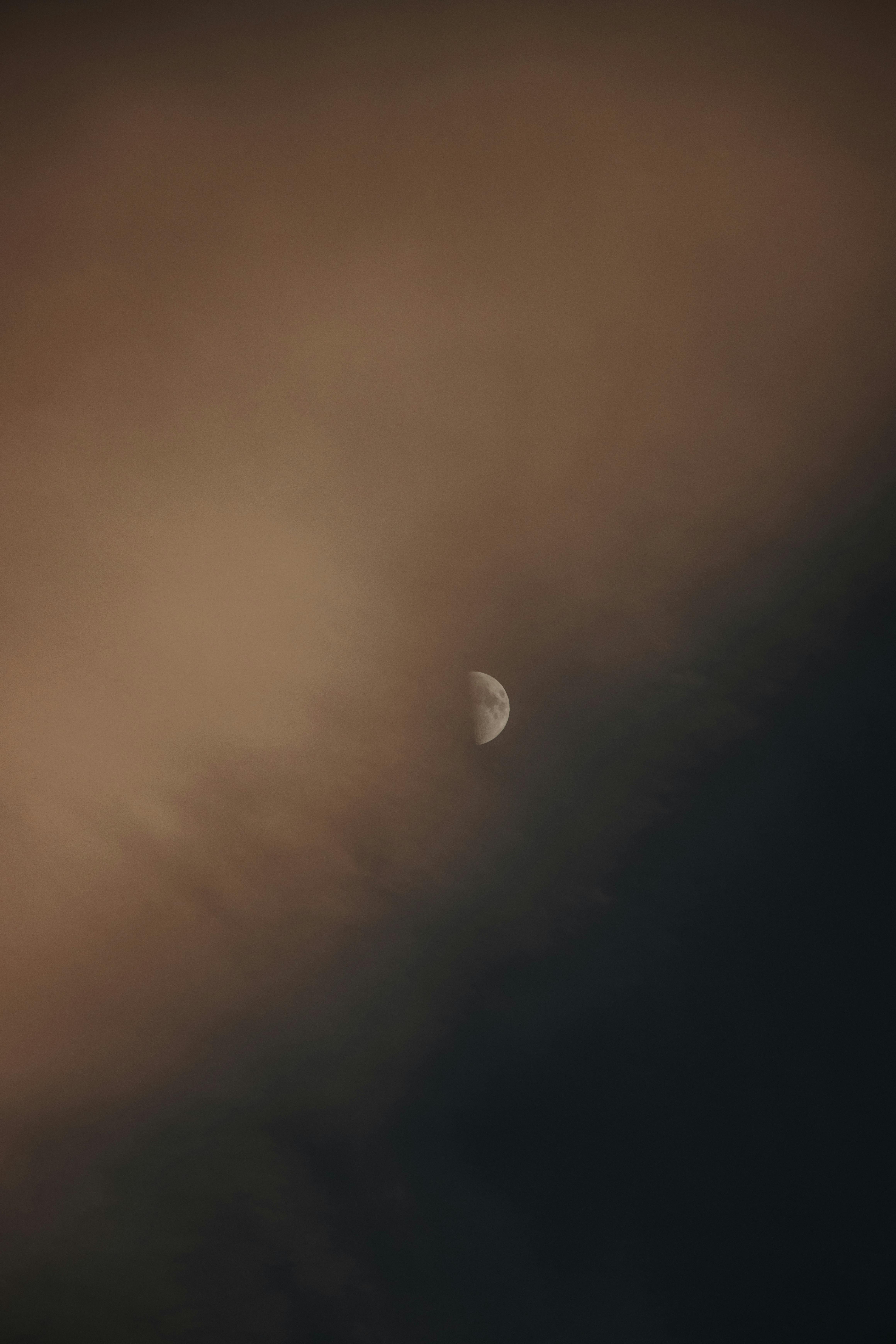 A calming view of the moon partly cloaked by soft clouds in a twilight sky.