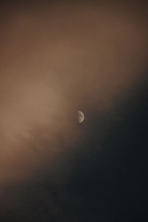 Free A calming view of the moon partly cloaked by soft clouds in a twilight sky. Stock Photo