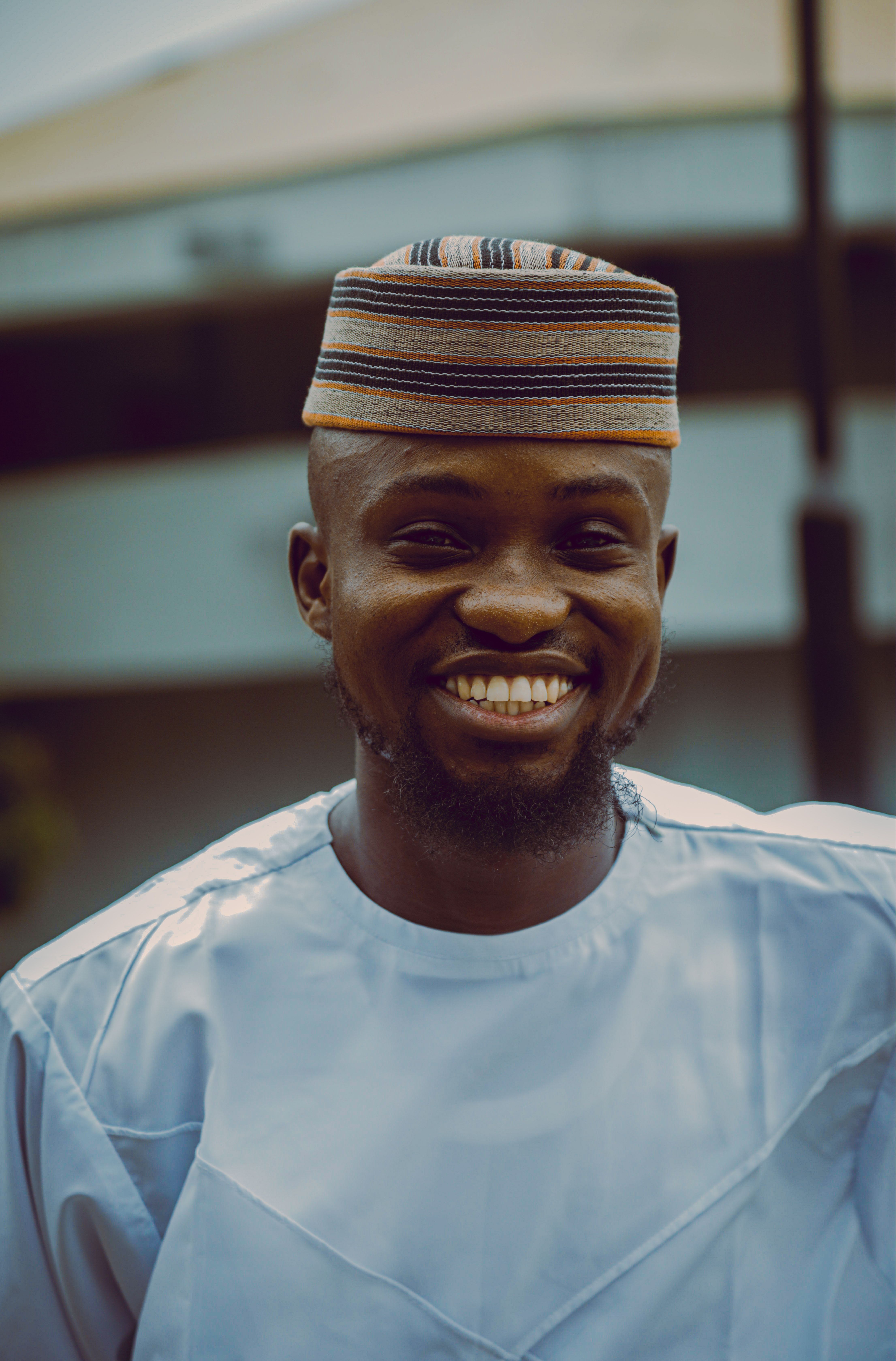 A cheerful African man in traditional attire smiles brightly outdoors.