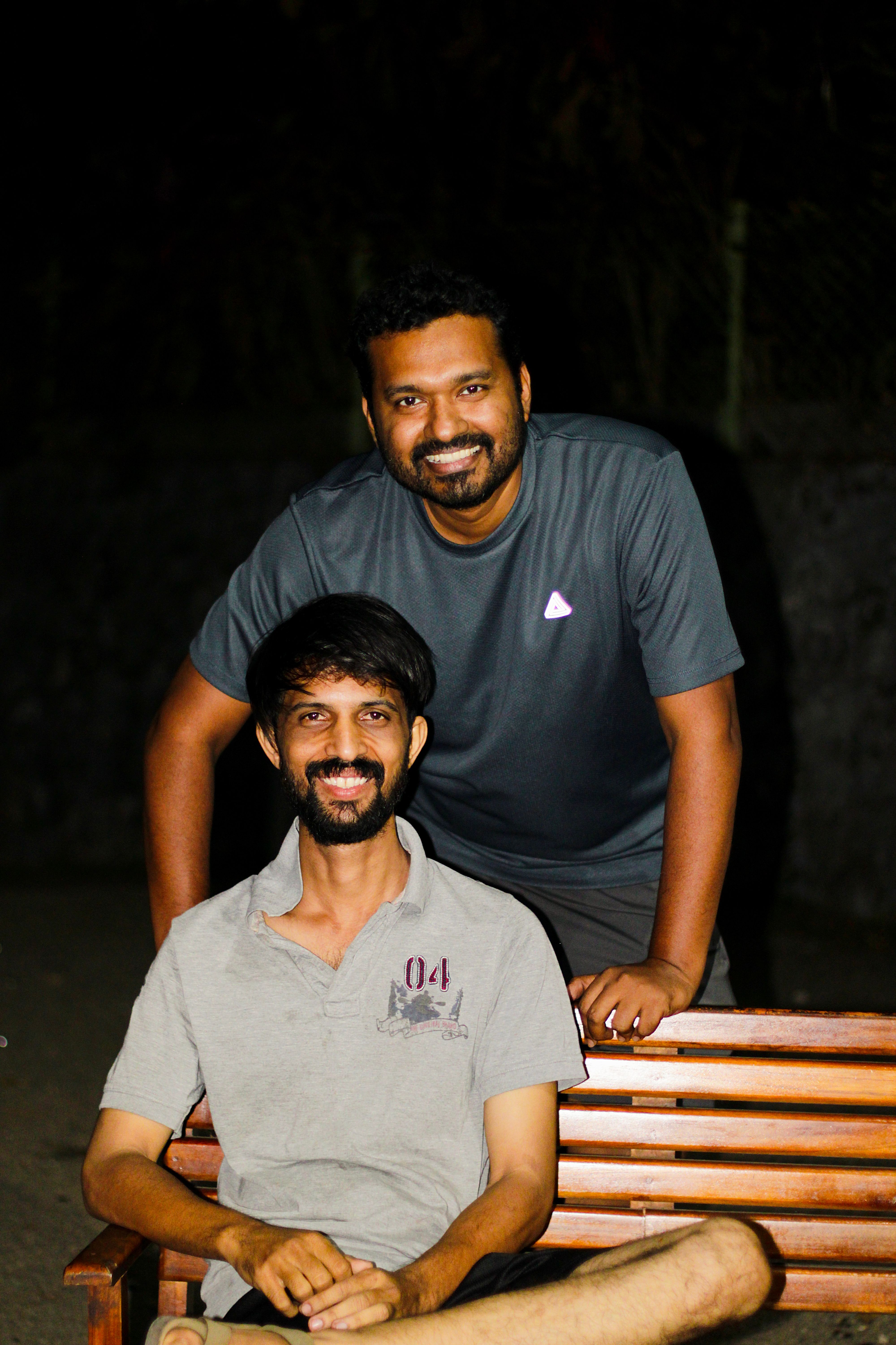 Two happy men posing on a bench at night, showcasing friendship and leisure outdoors.
