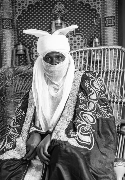 Free Black and white portrait of a person in traditional African attire with intricate patterns and a covered face. Stock Photo
