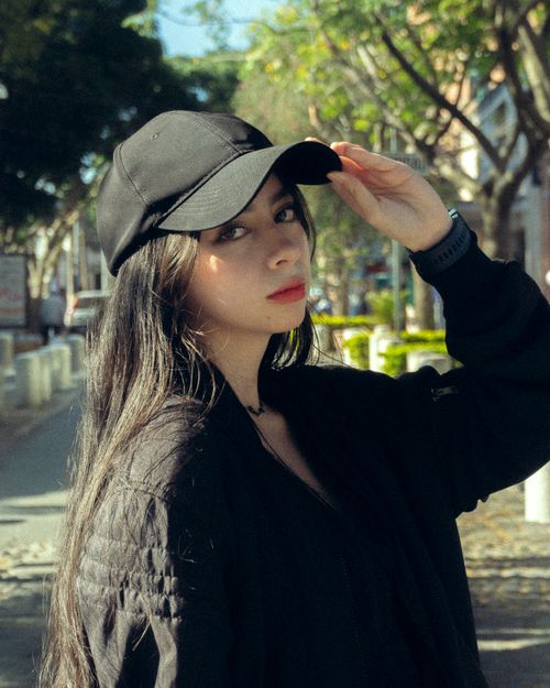 Free Young woman outdoors in casual wear, adjusting her black baseball cap. Stock Photo