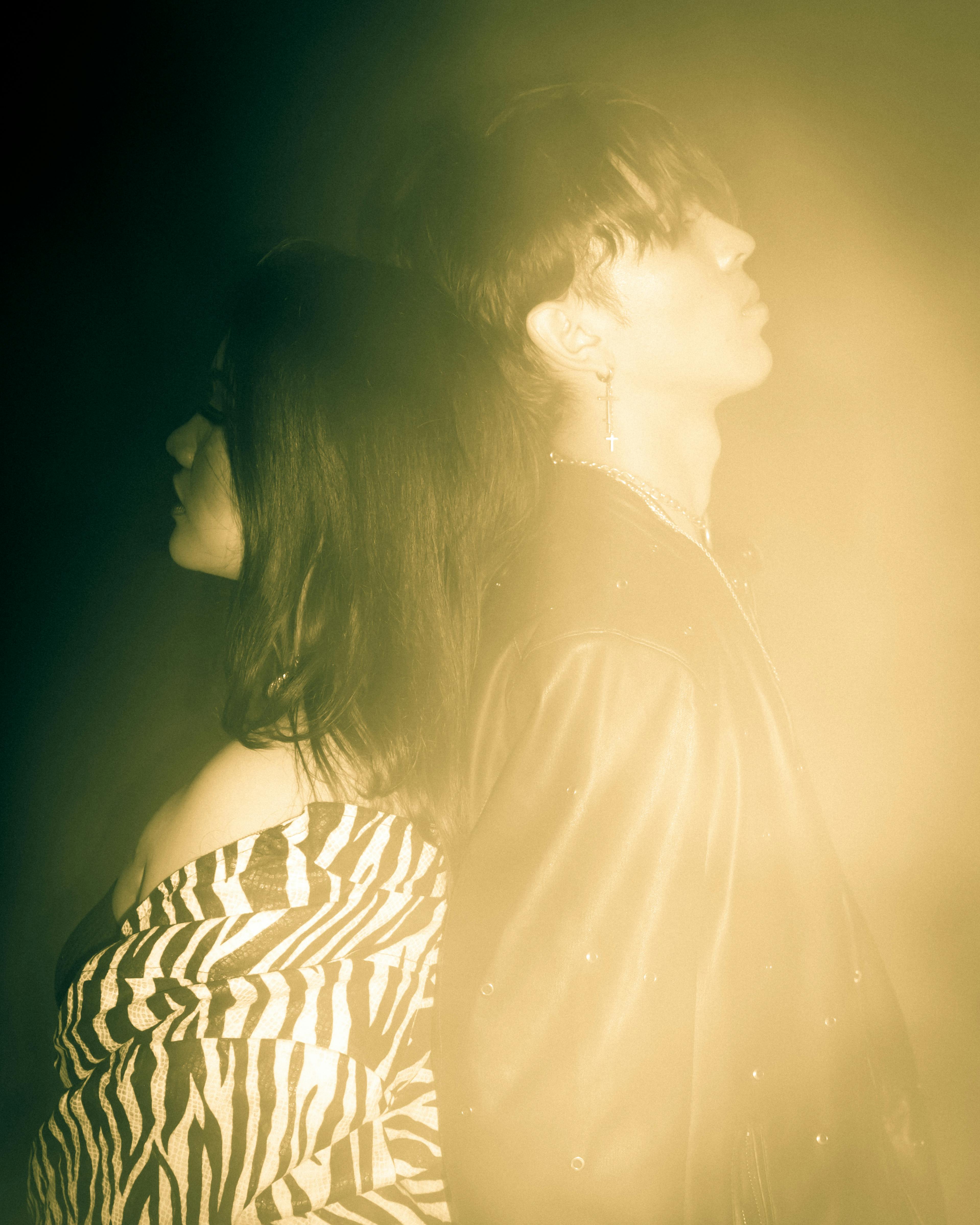 Artistic photo of two people standing back to back in a moody and dramatic lighting.