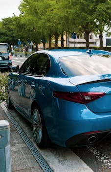 A sleek blue car parked on a city street under sunlight with green trees lining the road.