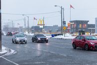 Winter street scene in Toronto with cars driving past McDonald's during snowfall.