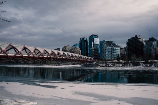 Scenic view of Calgary's Peace Bridge with city skyline and frozen river in winter.