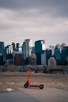 Orange electric scooter with Calgary's skyline as a backdrop on a cloudy day.
