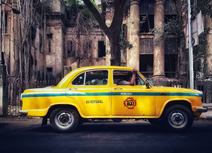 A classic yellow taxi parked in front of a dilapidated building, evoking nostalgia and urban charm.