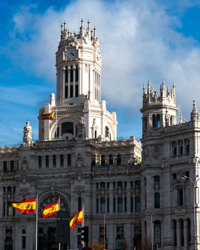 The iconic Palacio de Cibeles in Madrid with Spanish flags waving under a blue sky.