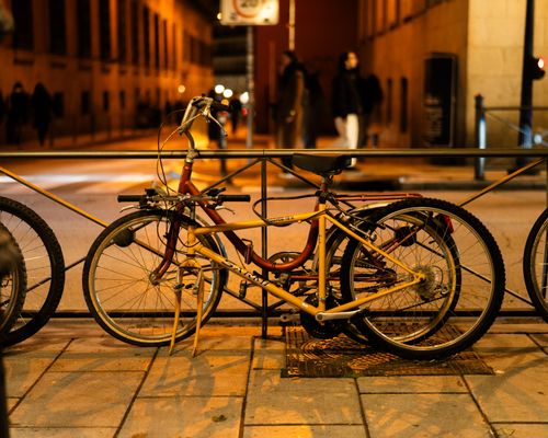 Free A bicycle parked against a railing on a city street at night, with people walking in the background. Stock Photo