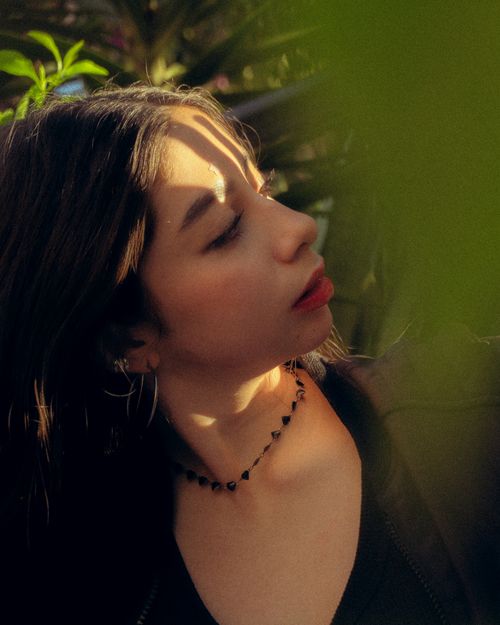 Free A contemplative woman captured in soft, natural sunlight with lush greenery in the background. Stock Photo