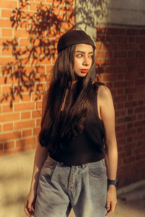 Free Stylish young woman in casual outfit posing against sunlit brick wall. Stock Photo