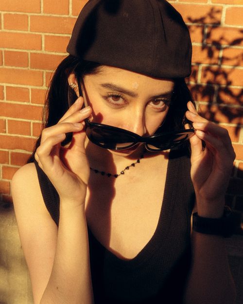 Free A fashionable woman wearing a beret and sunglasses poses confidently in warm sunlight against a brick wall. Stock Photo