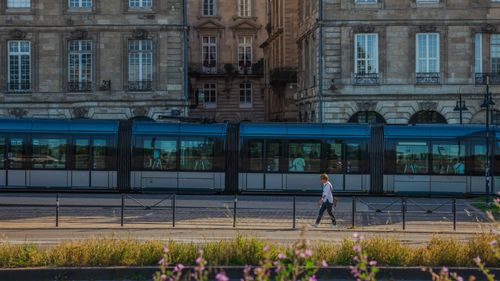 Free A commuter walks by a modern tram in Bordeaux, France, showcasing urban architecture. Stock Photo