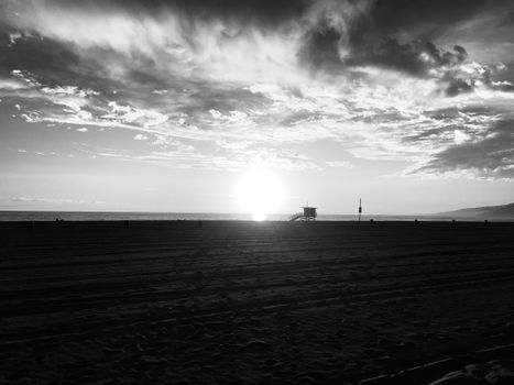 Dramatic black and white sunset over Santa Monica beach with a silhouetted lifeguard tower.