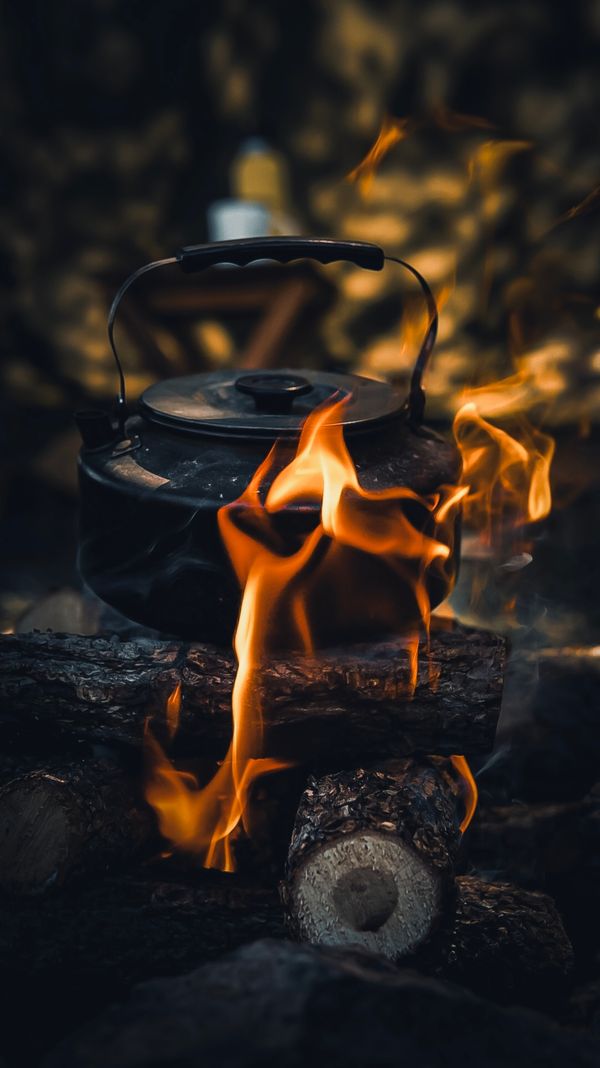 kettle boiling water over open campfire at campsite to purify hiking water