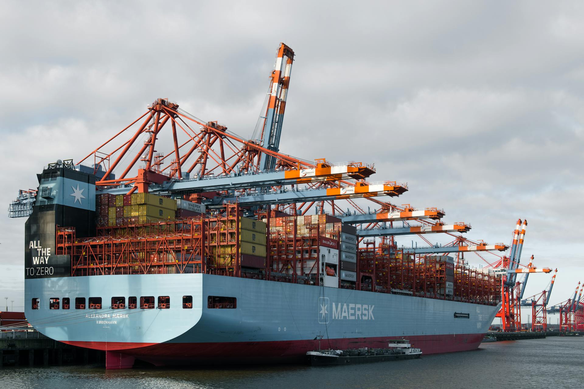 Container ship docked at Hamburg port being loaded by cranes.