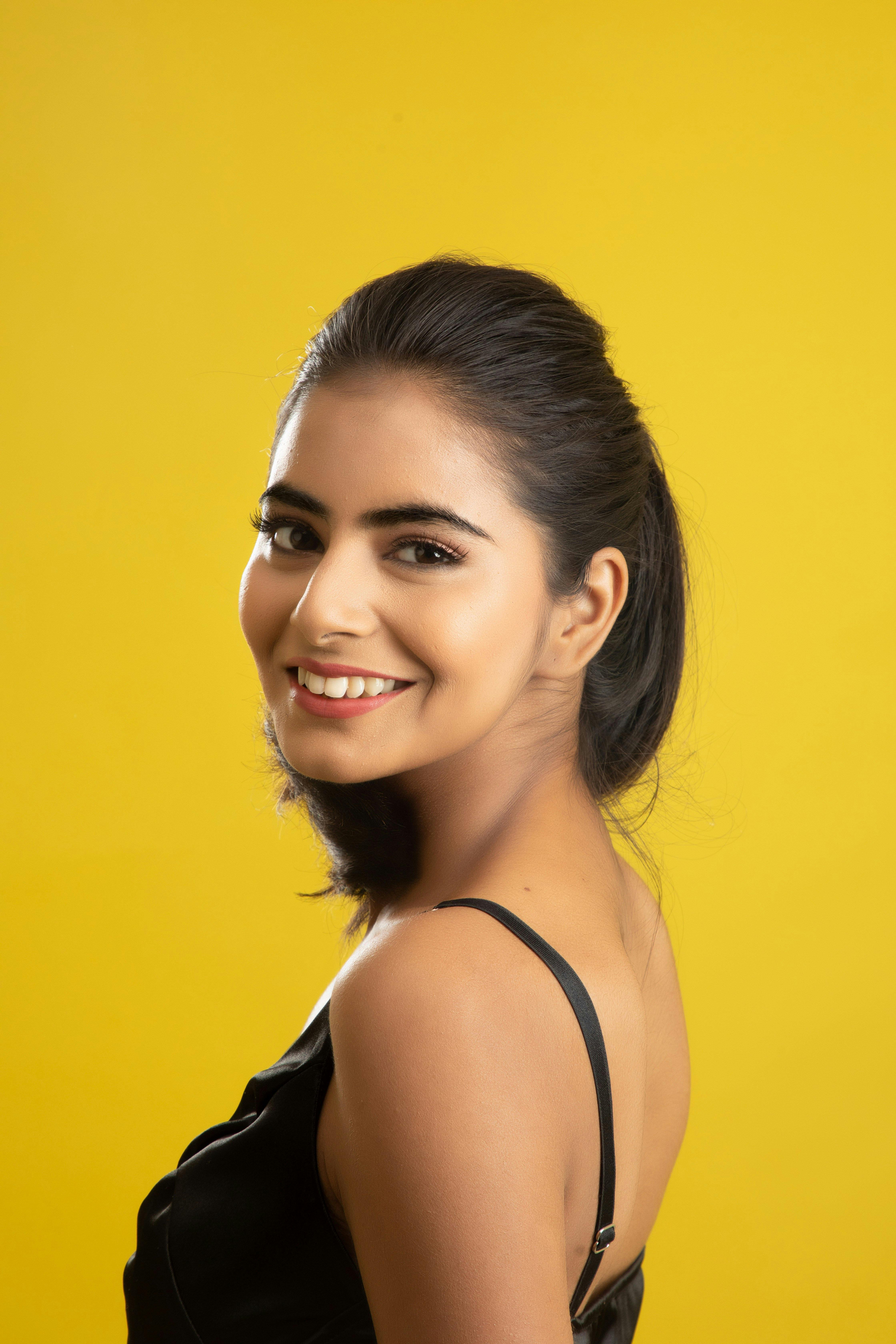 Portrait of a smiling woman with dark hair against a vibrant yellow backdrop.