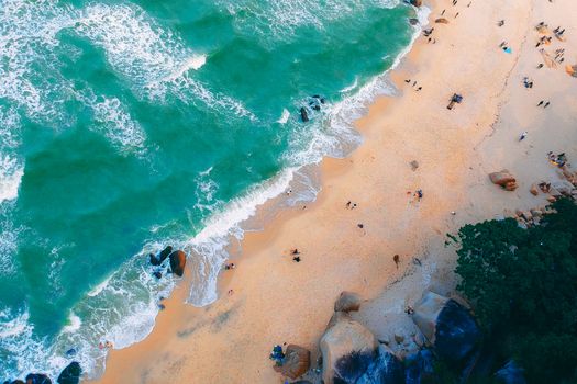 Stunning aerial shot capturing vibrant turquoise waves crashing on a sandy beach with scattered beachgoers.