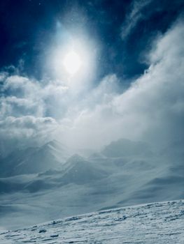 Sunlit snowy mountains under a dramatic sky, capturing winter's essence.