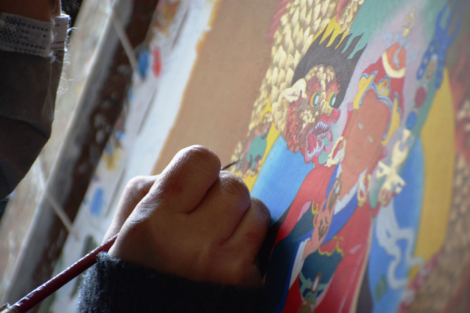 A painter's hand with a fine brush detailing a wrathful deity on a thangka in Sikkim