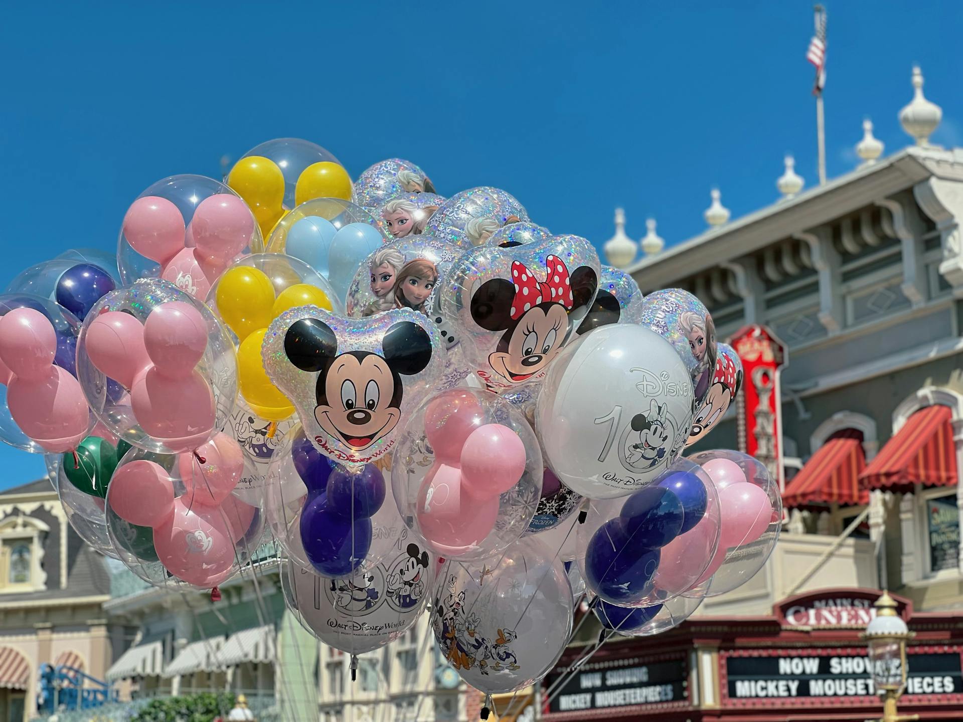 Vibrant Disney character balloons in front of theme park cinema under blue sky.