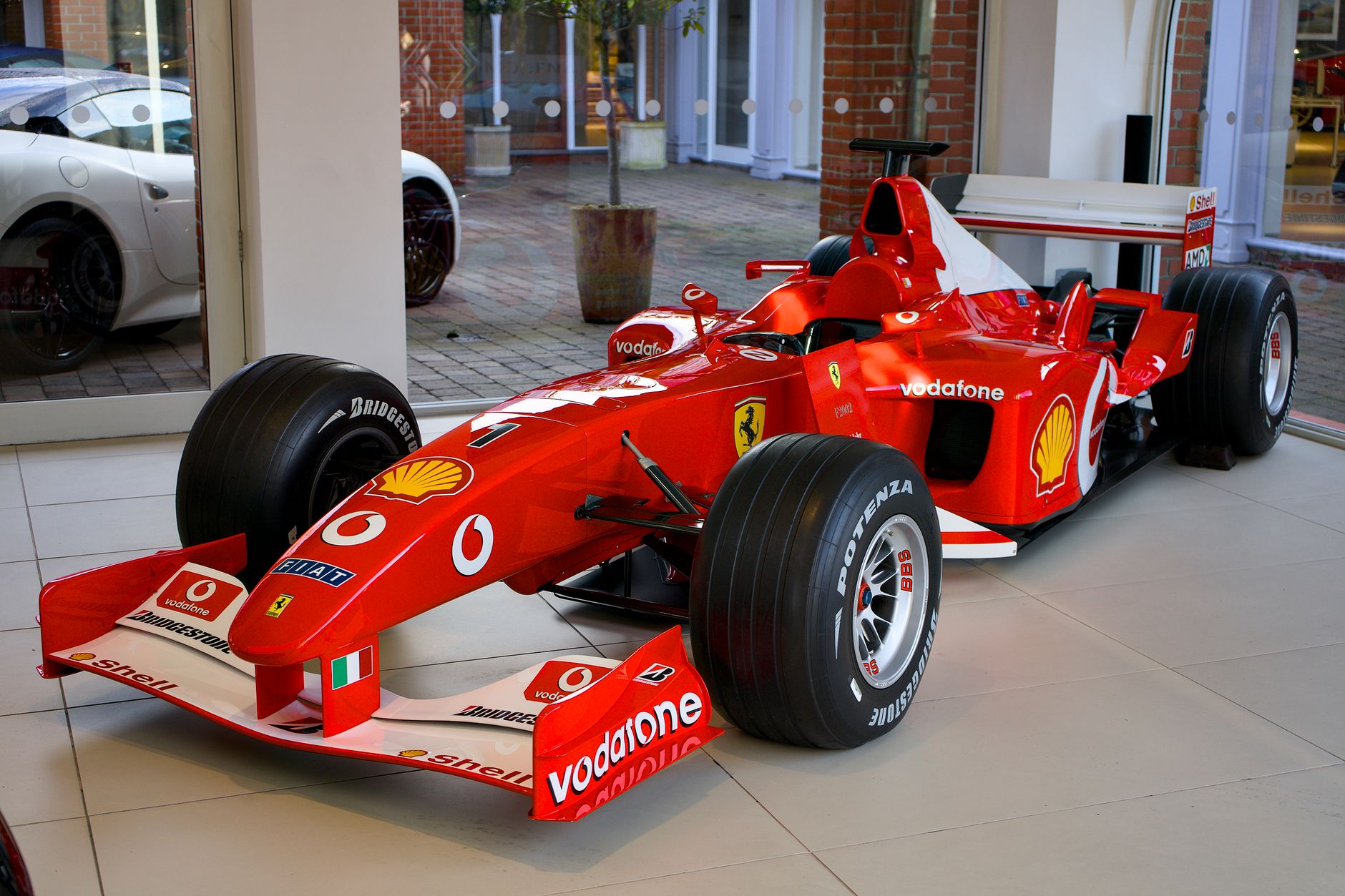 A striking red Formula 1 Ferrari race car displayed in a modern showroom setting.