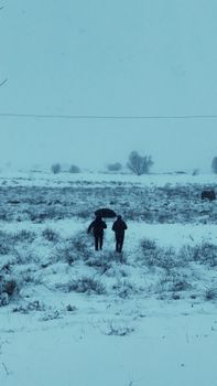 Two people walking in the snowy fields of Cappadocia, Turkey, under cloudy skies.