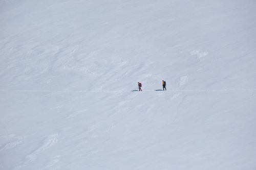 Free Two hikers trekking across a vast, snowy alpine landscape captured in a minimalist style. Stock Photo