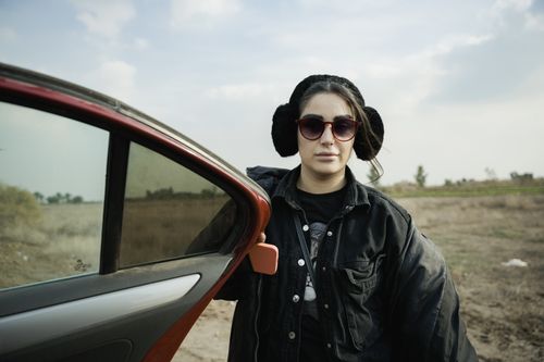 Free Woman wearing sunglasses and earmuffs, standing by a car in a rural area. Stock Photo