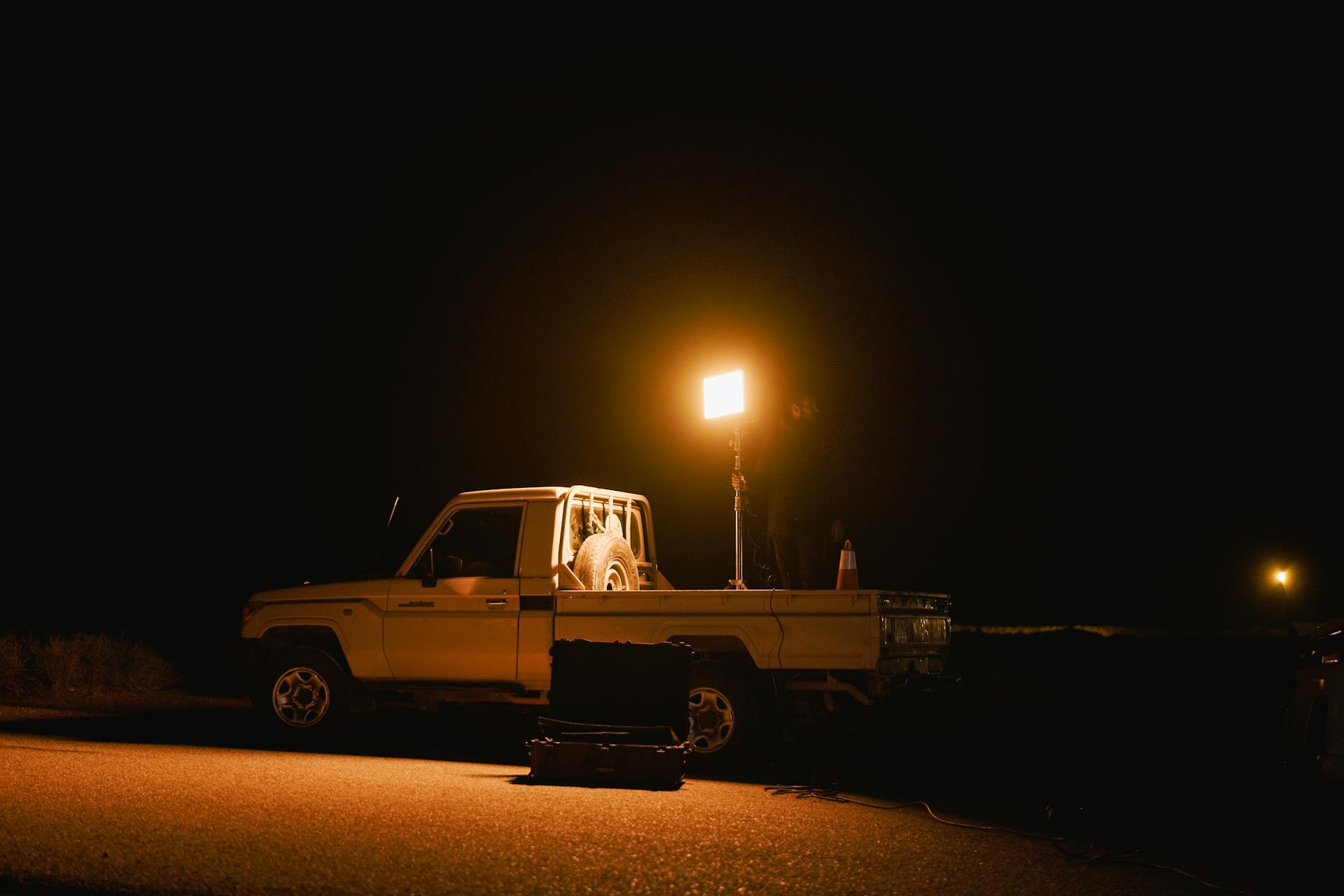 A white truck with a spotlight illuminating the road at night, creating a dramatic scene.