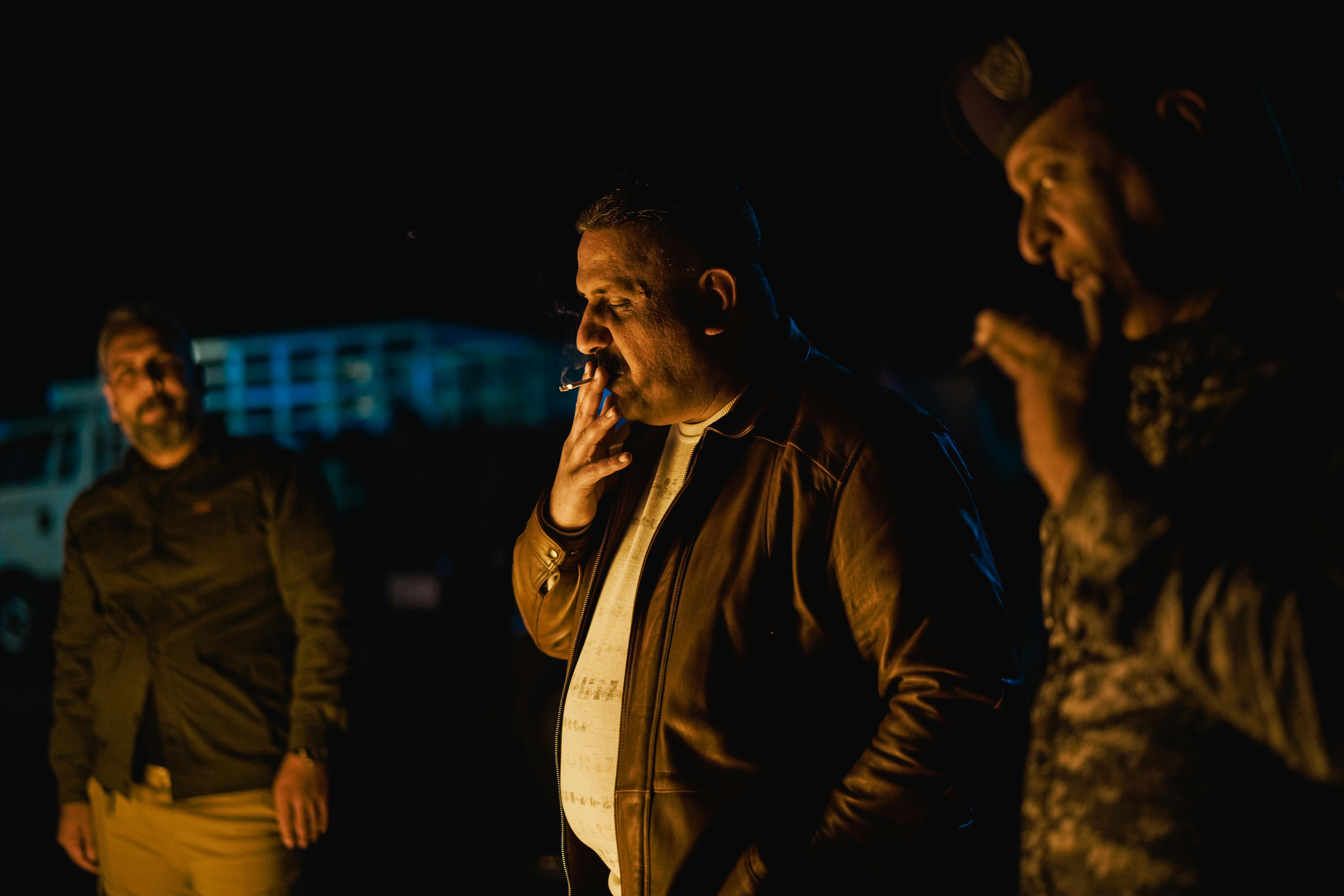 Group of men enjoying a relaxed outdoor gathering at night, smoking cigars and socializing.